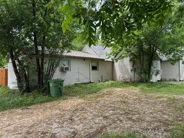 a backyard of a house with plants and large tree