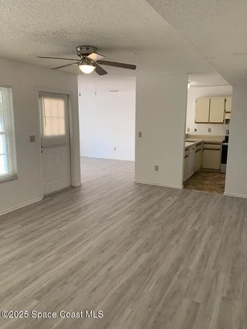an empty room with wooden floor kitchen view and windows