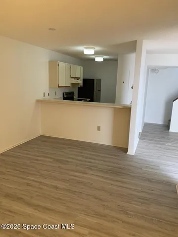 a view of kitchen and empty room with wooden floor