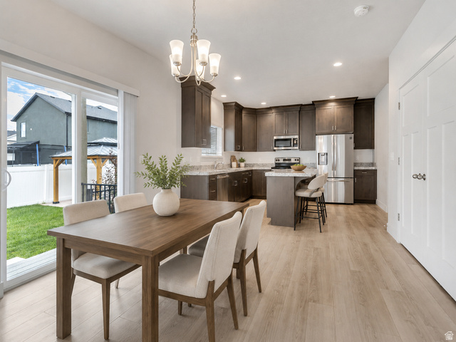 4572 Flower Point Eagle Mountain, UT 84005 - Photo 16 of 62 Open-concept kitchen and dining area featuring light wood-finish flooring, dark wood cabinetry, stainless steel appliances, and a kitchen island with seating