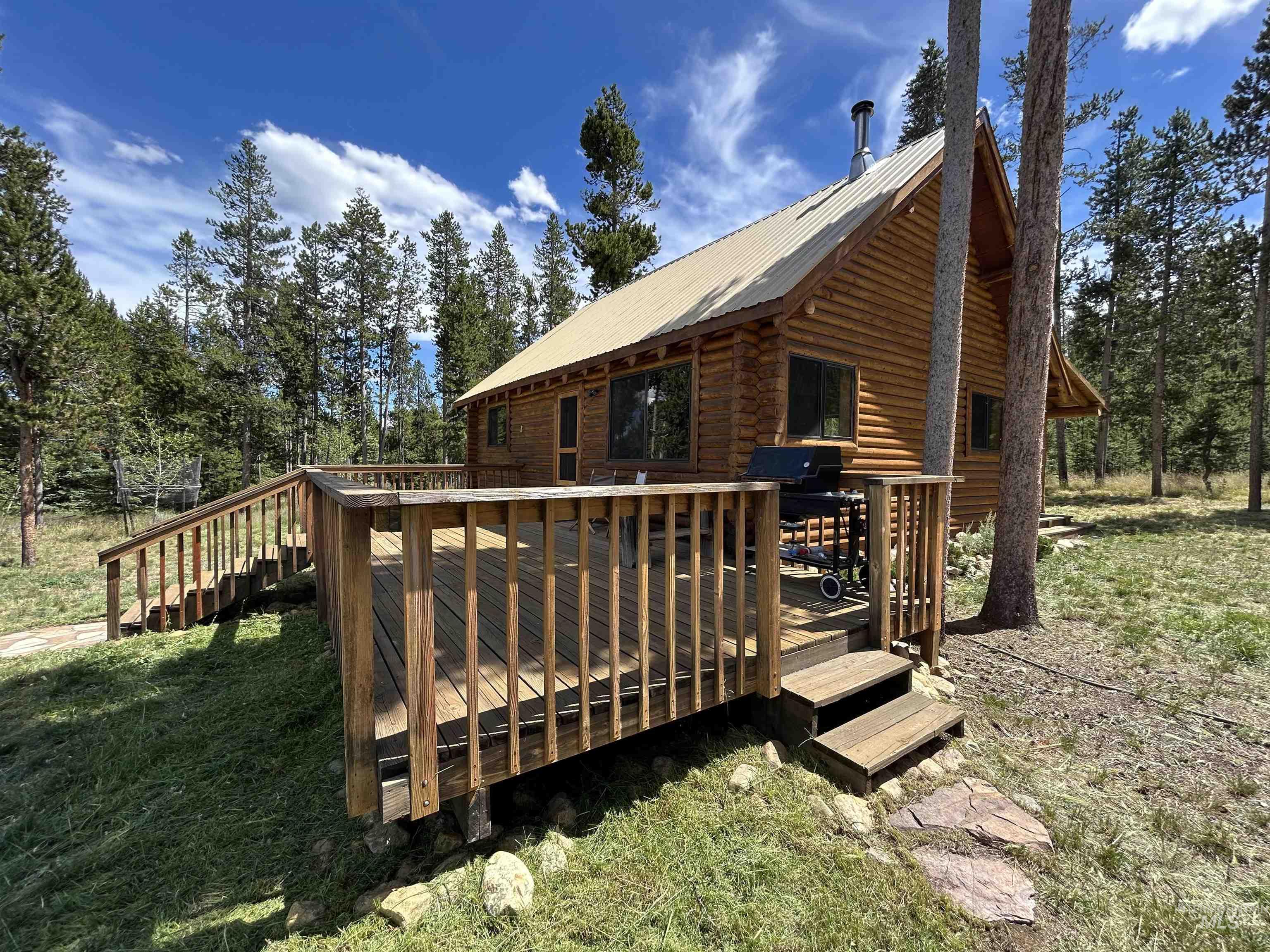 35 Sawtooth Way Stanley, ID 83278 - Photo 3 of 36 Log cabin exterior featuring a spacious wooden deck with railings, a metal roof, and surrounding mature trees