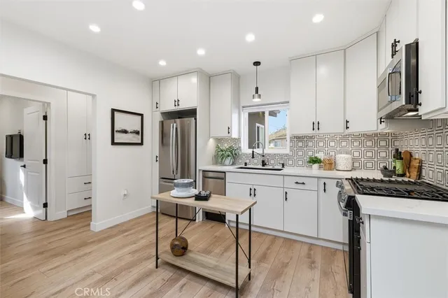 a kitchen with stainless steel appliances granite countertop a refrigerator a sink dishwasher a stove and white cabinets with wooden floor