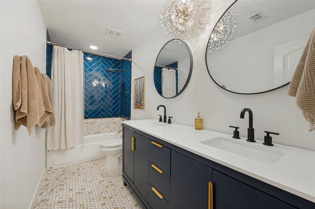 3619 Merrell Road Dallas, TX 75229 - Photo 15 of 26 Bathroom featuring a dual vanity with a white countertop and matte black fixtures, round mirrors, and a tub with a blue herringbone tile surround