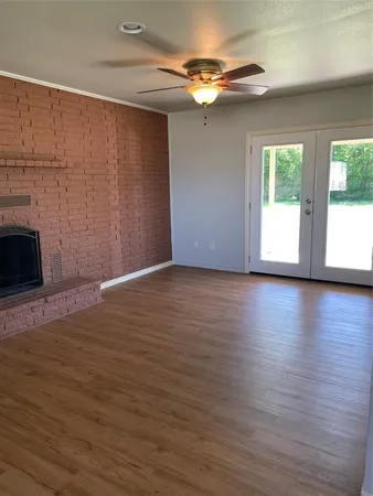 a view of an empty room with wooden floor fireplace and a window
