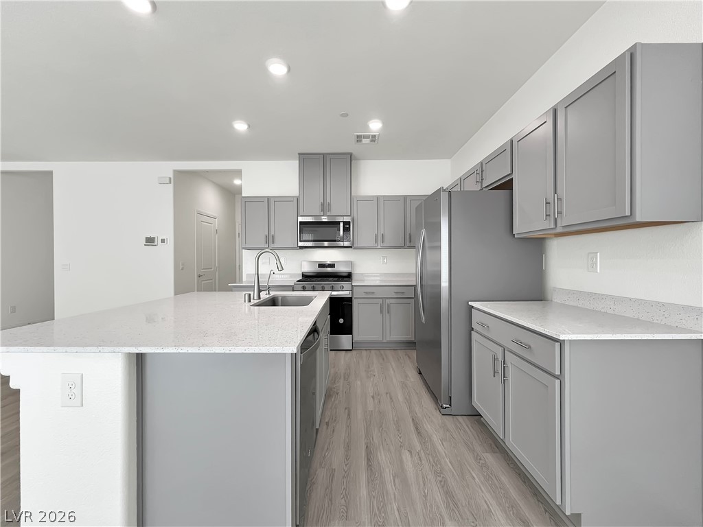 9984 Indigo Cliffs Street Las Vegas, NV 89141 - Photo 5 of 31 Kitchen featuring an island with sink, a sink, gray cabinetry, light wood-style floors, and appliances with stainless steel finishes