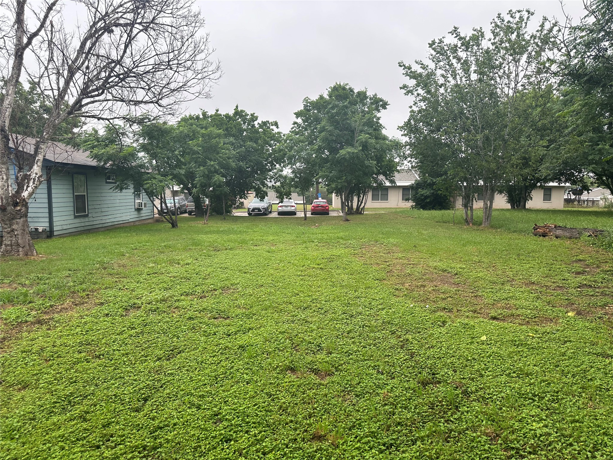 608 Lamar Street Luling, TX 78648 - Photo 3 of 7 Expansive grassy lot featuring mature trees and a partial view of a light blue-sided structure with an exterior air conditioning unit