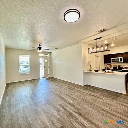 an empty room with wooden floor kitchen view and windows