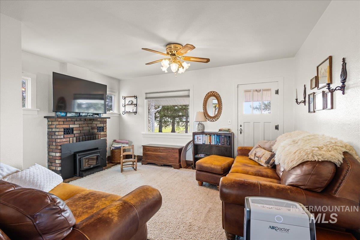 19454 Idaho Road Worley, ID 83876 - Photo 16 of 39 Living area featuring a brick fireplace with a wood-burning insert, multiple windows, and a ceiling fan with integrated lighting
