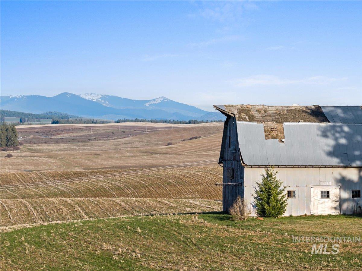 19454 Idaho Road Worley, ID 83876 - Photo 6 of 39 Barn structure with a gambrel roof and corrugated metal siding, situated in a field with distant snow-capped mountains
