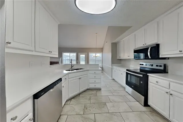 a kitchen with stainless steel appliances granite countertop a sink a stove top oven and white cabinets