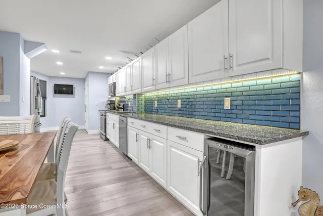 a kitchen with stainless steel appliances granite countertop a stove top oven a sink dishwasher and white cabinets with wooden floor