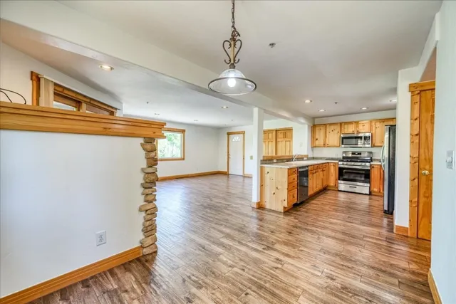 a view of a kitchen with kitchen island wooden floor stainless steel appliances and cabinets