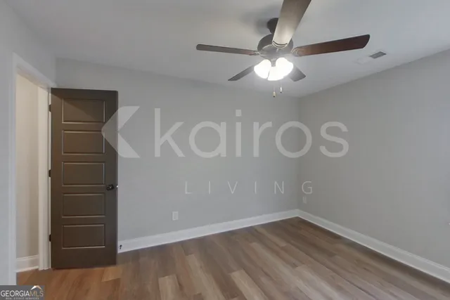a view of an empty room with wooden floor and a ceiling fan