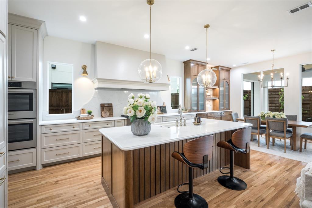 3304 Ferguson Road Grapevine, TX 76092 - Photo 18 of 38 Open-concept kitchen featuring a large central island with a solid surface countertop, wood-finish flooring, integrated double ovens, recessed lighting, and elegant pendant fixtures
