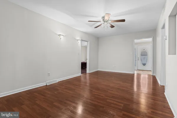 a view of an empty room with wooden floor and a ceiling fan
