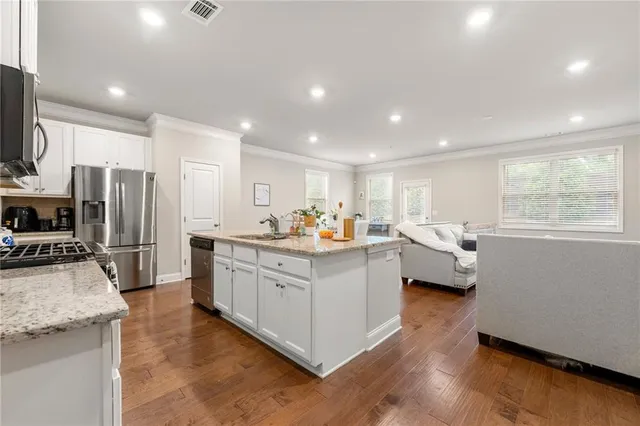 a large white kitchen with stainless steel appliances granite countertop a large counter top a sink dishwasher a stove and a refrigerator with wooden floor