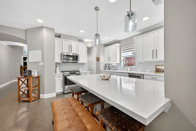 a kitchen with stainless steel appliances granite countertop a refrigerator a sink dishwasher a stove and white cabinets with wooden floor