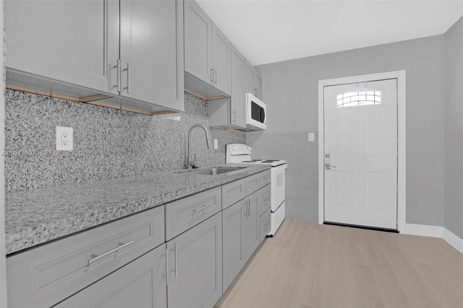 369 Phippen Waiters Road, Unit 2 Dania Beach, FL 33004 - Photo 9 of 18 a kitchen with granite countertop white cabinets and sink