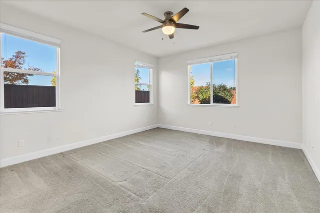 an empty room with chandelier fan and kitchen view
