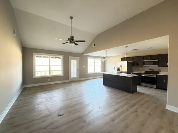 a living room with stainless steel appliances kitchen island granite countertop a stove a refrigerator a sink a dining table and chairs with wooden floor