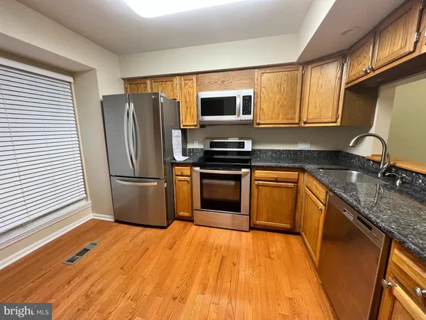 a kitchen with stainless steel appliances granite countertop a stove a sink dishwasher a refrigerator and a microwave oven with wooden floor