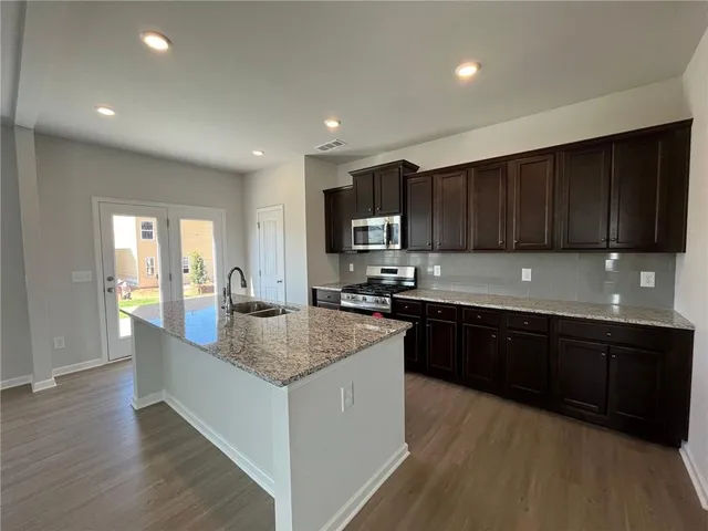 a kitchen with granite countertop wooden cabinets a sink dishwasher and a stove with wooden floor