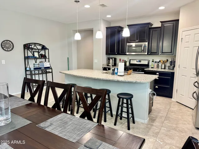 a kitchen with stainless steel appliances kitchen island granite countertop a refrigerator a stove a sink a dining table and chairs with wooden floor