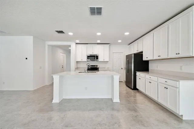 a large white kitchen with stainless steel appliances granite countertop a stove a sink a refrigerator and white cabinets