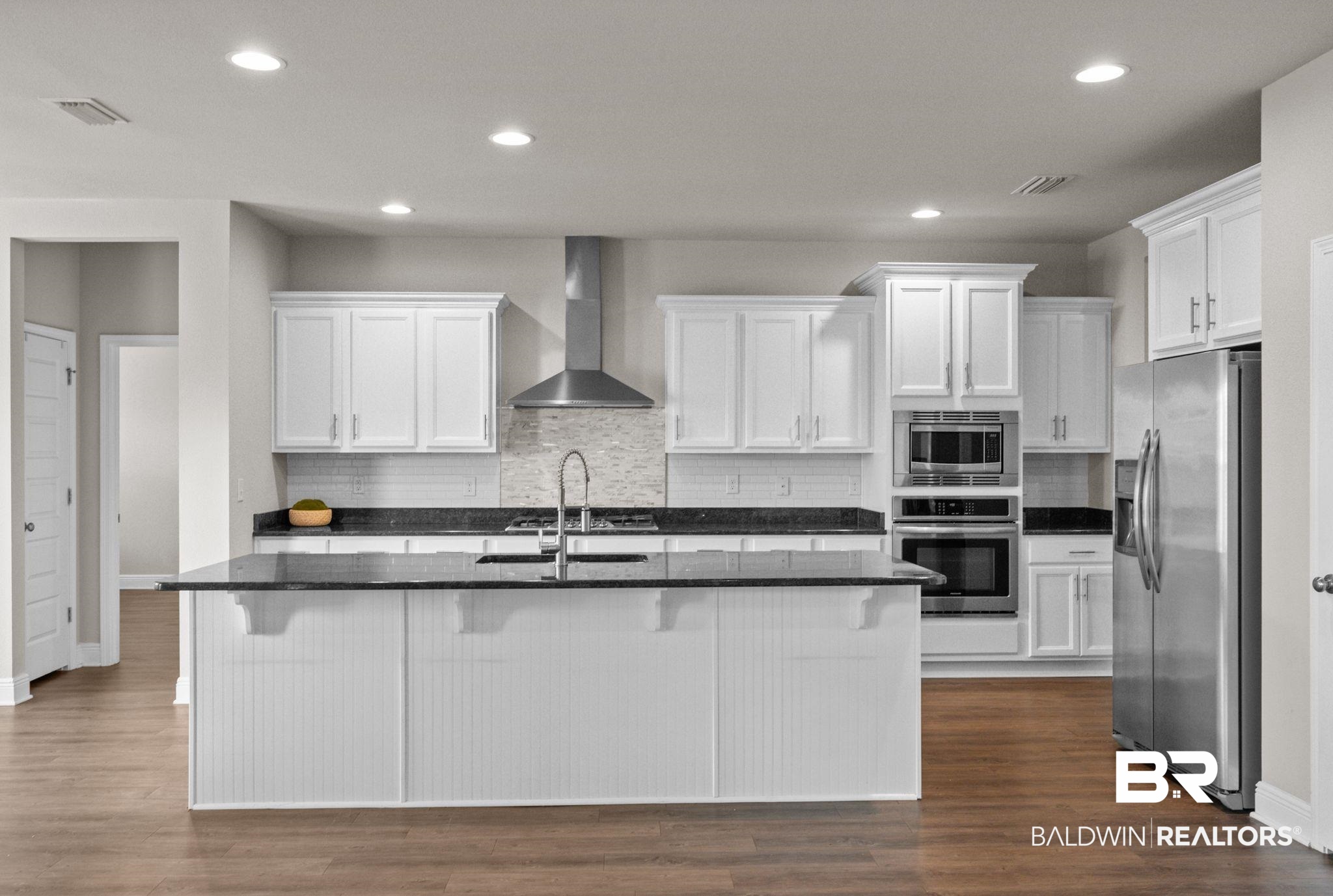 2074 Bourbon Street Foley, AL 36535 - Photo 6 of 46 Kitchen featuring appliances with stainless steel finishes, a kitchen island with sink, white cabinetry, dark wood-type flooring, and wall chimney exhaust hood