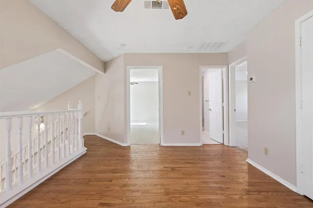 an empty room with wooden floor ceiling fan and windows