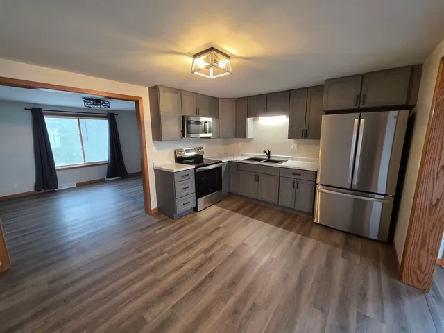 a kitchen with a refrigerator a sink dishwasher a kitchen island with wooden floor and cabinets