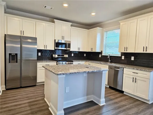 a kitchen with stainless steel appliances granite countertop a stove a sink a refrigerator a white cabinets and wooden floor