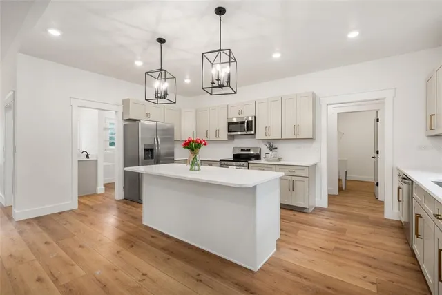 a kitchen view with stainless steel appliances a stove top oven a refrigerator a center island a wooden floor and white cabinets