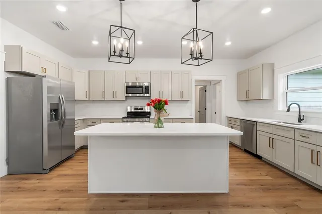 a kitchen with stainless steel appliances kitchen island granite countertop a sink a stove a refrigerator and island with wooden floor