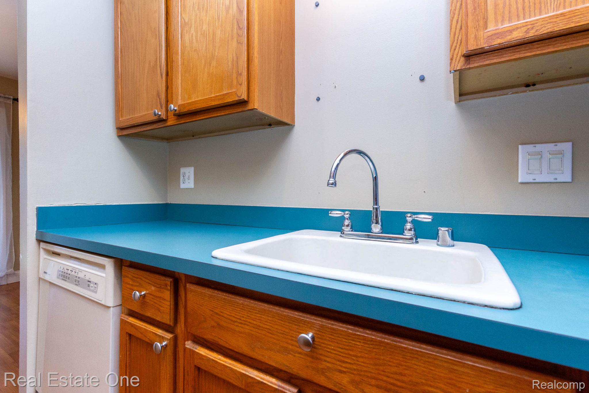111 Manor Way Rochester, MI 48309 - Photo 13 of 36 Kitchen sink area featuring a white drop-in basin, chrome faucet, blue countertops, and wood cabinetry