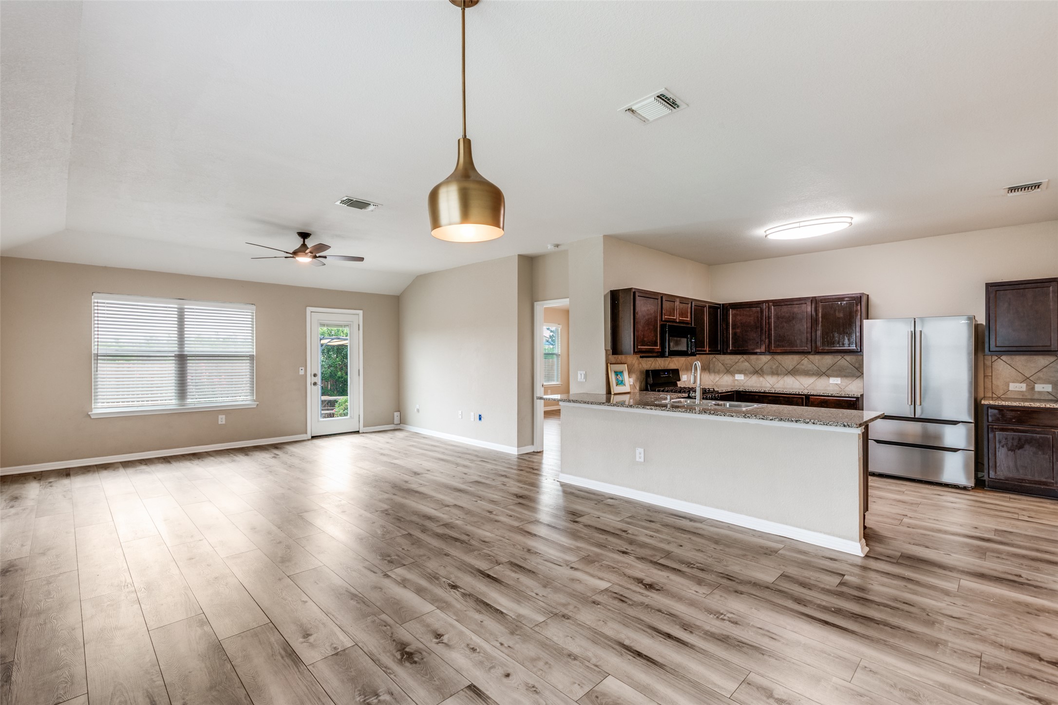2909 Centrum Drive Austin, TX 78754 - Photo 9 of 30 Open concept living area with light-colored flooring, a modern hanging light fixture, and a kitchen featuring dark cabinetry, stainless steel appliances, and a granite-topped island