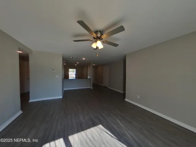a view of an empty room with wooden floor and a ceiling fan