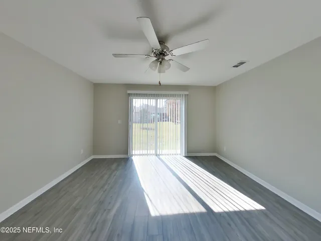 an empty room with wooden floor fan and windows