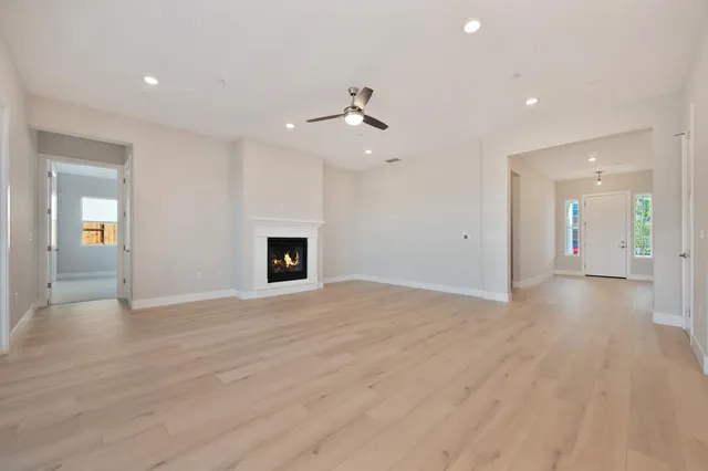 an empty room with wooden floor ceiling fan and kitchen view