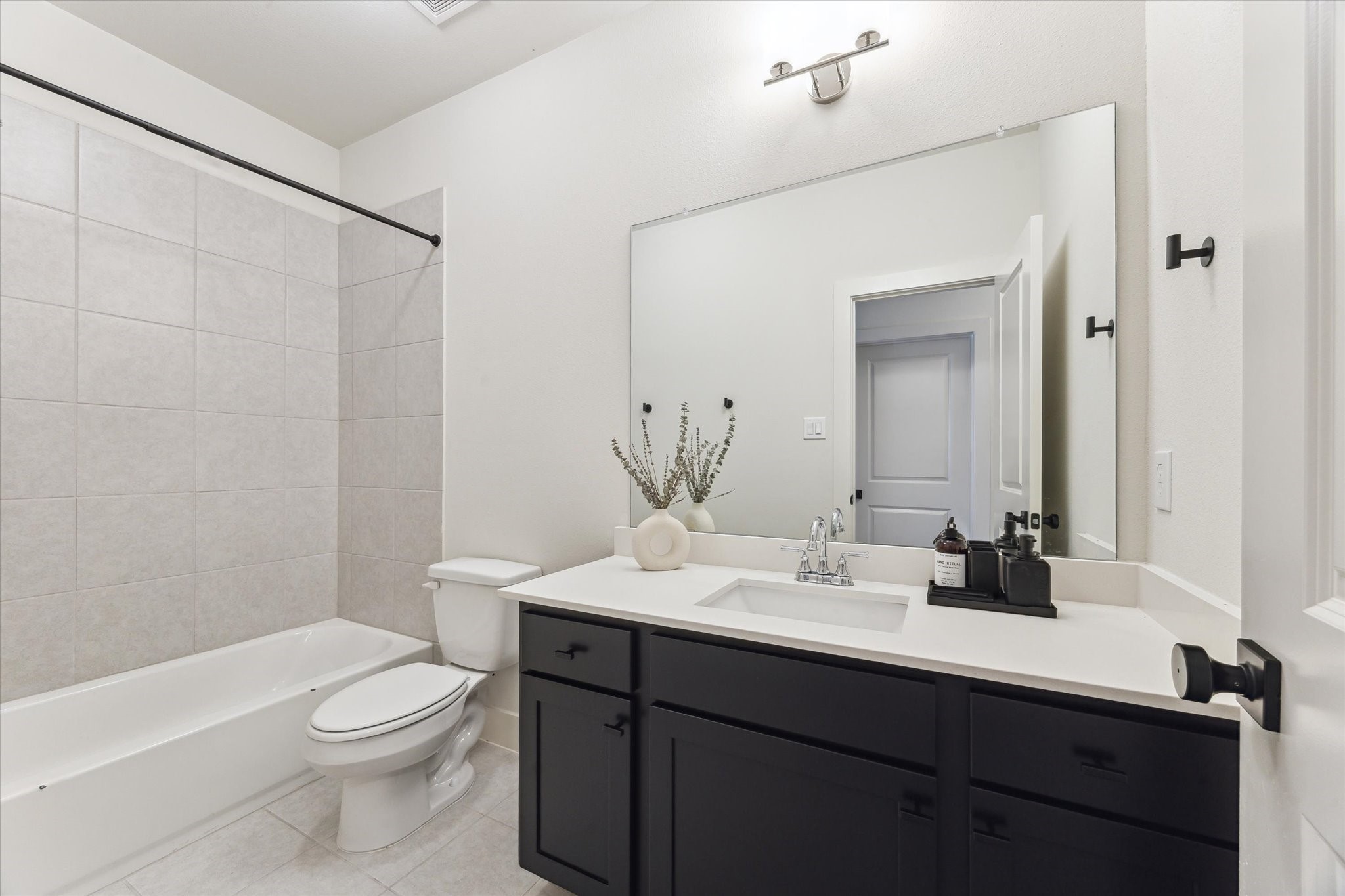 4155 Griggs Road Houston, TX 77021 - Photo 13 of 17 Bright secondary bathroom featuring a tub/shower combo, sleek white quartz countertops, and striking black cabinetry.