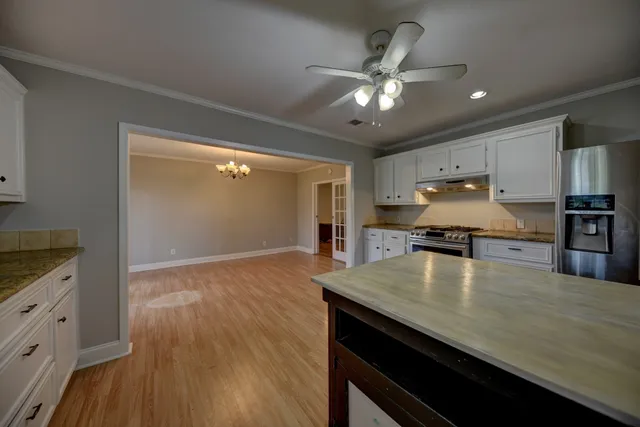 a view of an empty room with wooden floor and kitchen view