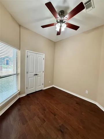 an empty room with wooden floor chandelier fan and windows