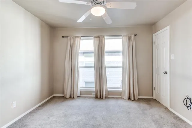 an empty room with chandelier fan and windows