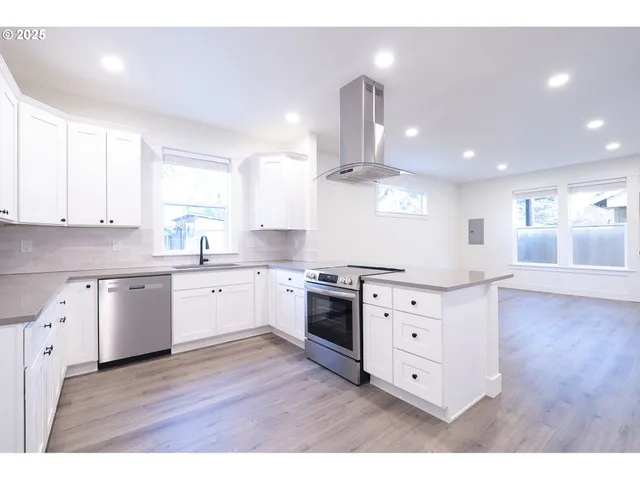 a kitchen with stainless steel appliances kitchen island a sink dishwasher a stove and white cabinets with wooden floor