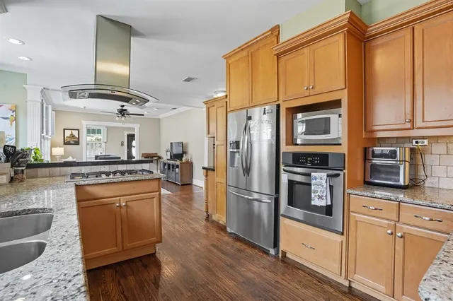 a kitchen with stainless steel appliances granite countertop a refrigerator a stove and a sink with wooden floors
