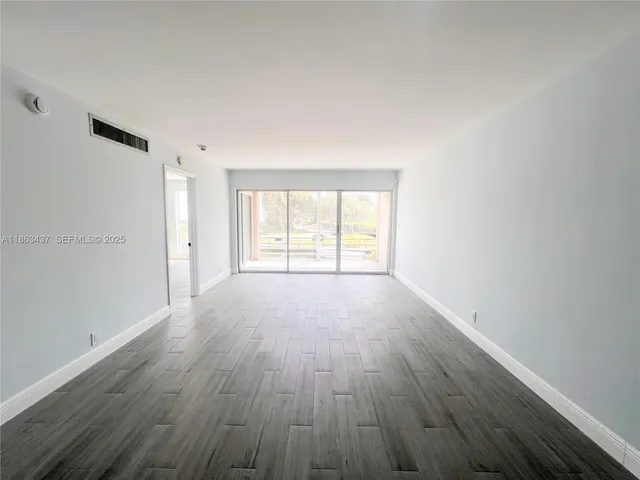 a view of an empty room with wooden floor and window