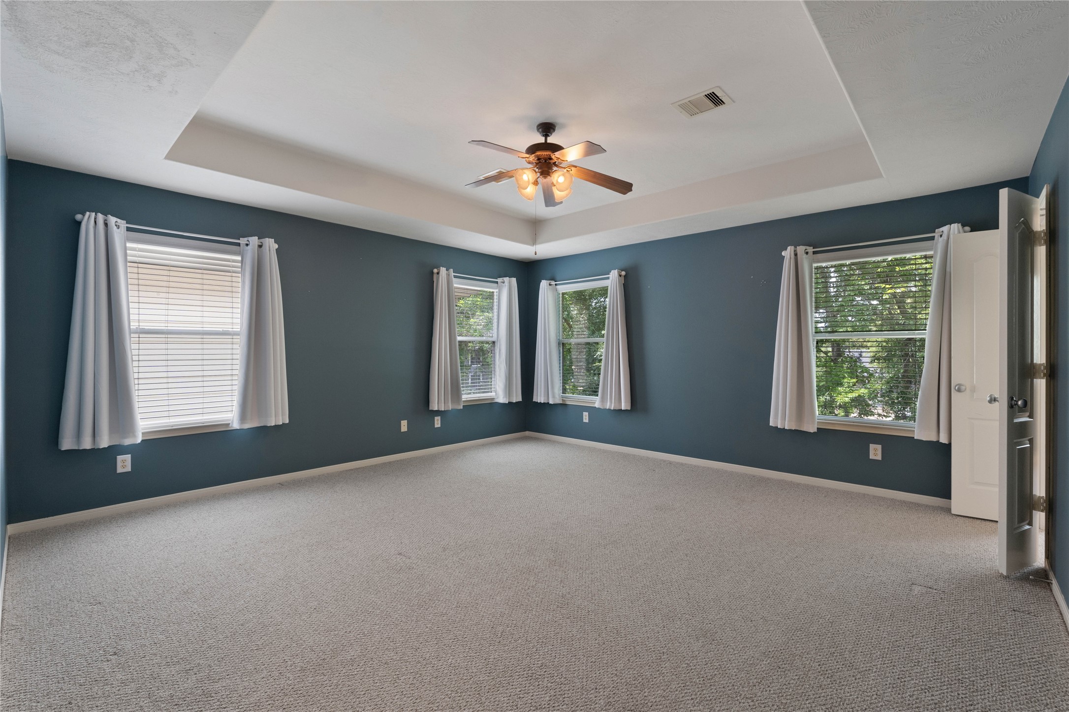 7414 Hollister Spring Houston, TX 77040 - Photo 15 of 26 Spacious primary bedroom with abundant natural light, featuring a stylish tray ceiling and a ceiling fan for added comfort.