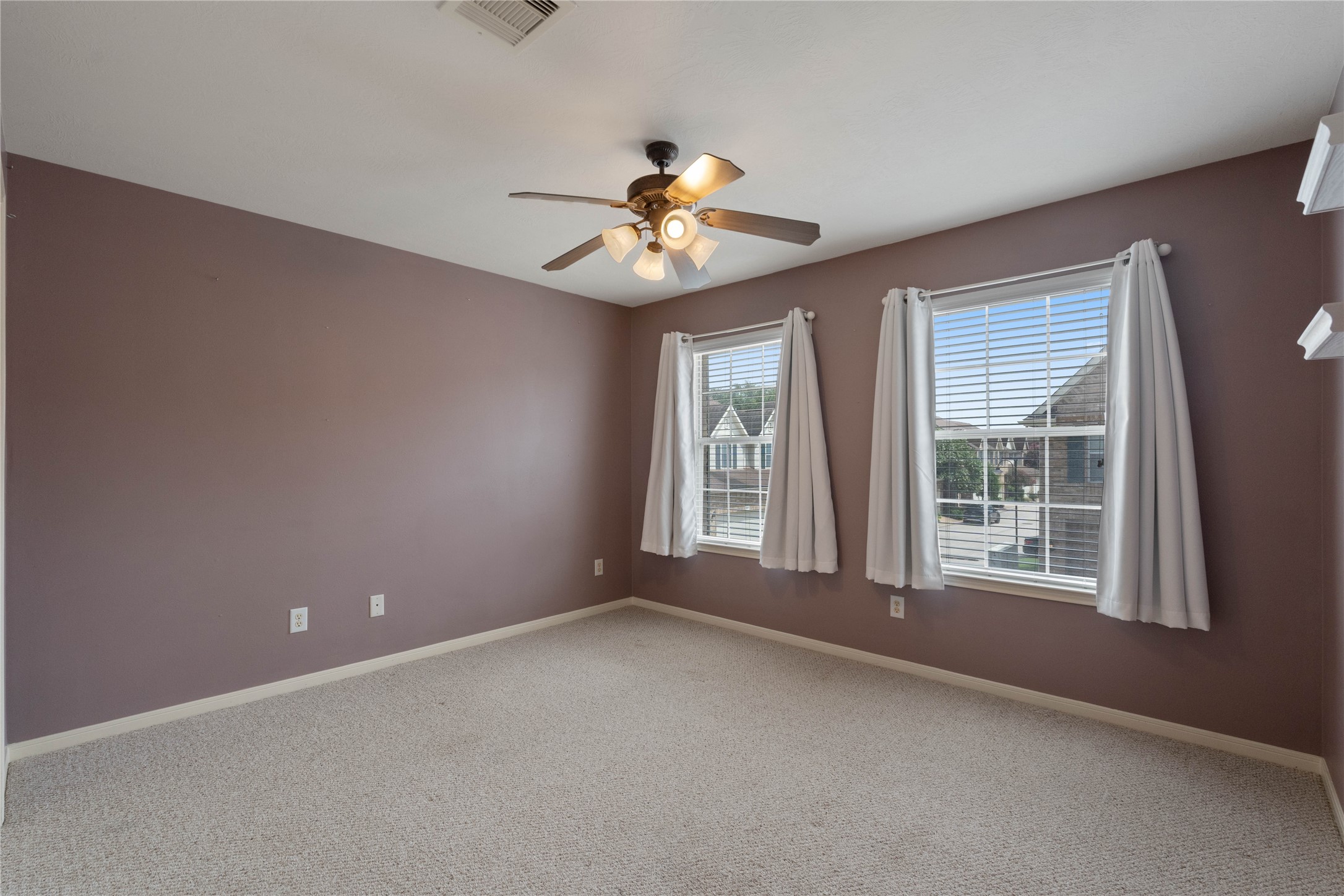 7414 Hollister Spring Houston, TX 77040 - Photo 24 of 26 This is a bright bedroom with soft purple walls and two large windows letting in plenty of natural light. It has a ceiling fan and light fixture, neutral carpet, and simple white curtains for a cozy feel.