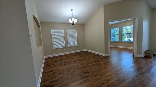 an empty room with wooden floor chandelier and windows