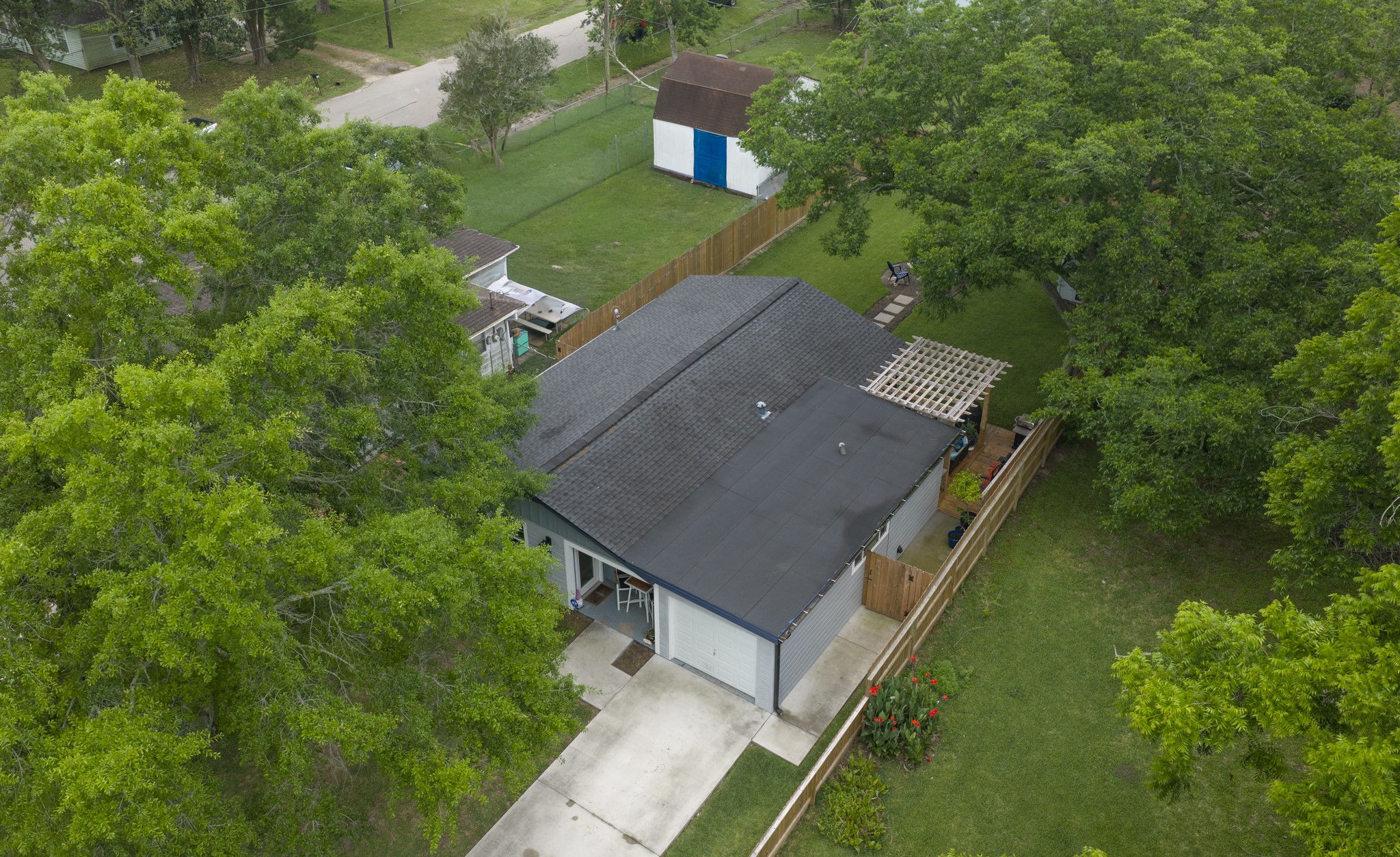 846 South Anderson Street Angleton, TX 77515 - Photo 30 of 30 This aerial view showcases a charming home with a dark new roof and a spacious yard, surrounded by lush greenery. The property includes a driveway, a fenced backyard, and a small shed, offering privacy and outdoor space in a serene neighborhood.